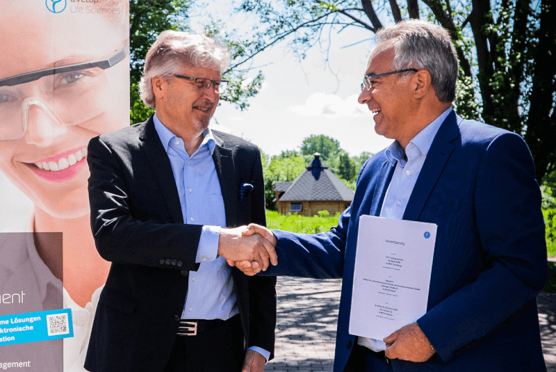 Illustration of the signing of the contract between Mr. Schnettler of PTS and Mr. Gukelberger of Digital Life Sciences