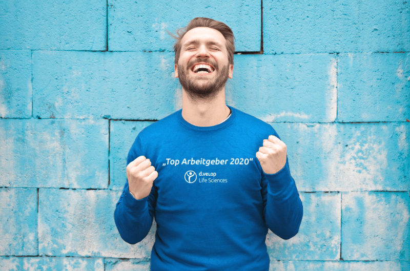 Person vor einer Mauer mit einem blauen Pullover auf dem steht Top Arbeitgeber Mittelstand